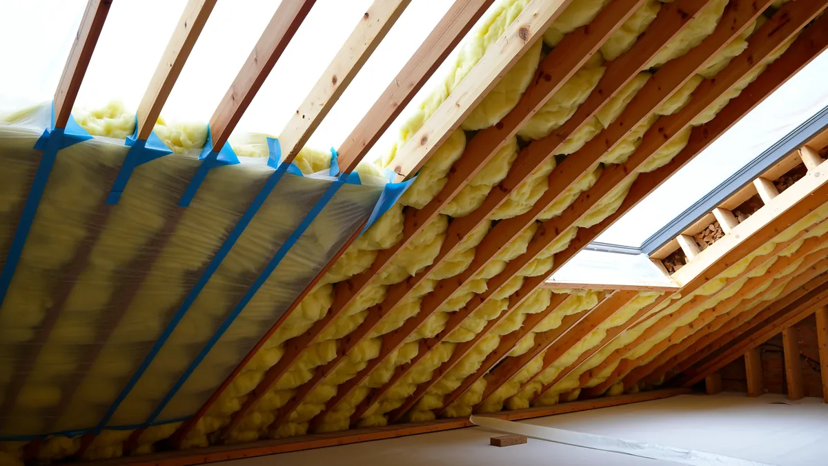 Dachgeschoss im Ausbau mit Mineralwolle zwischen den Holzsparren und einer teilweise verlegten Dampfbremsfolie, deren Stöße mit Klebeband verklebt sind
