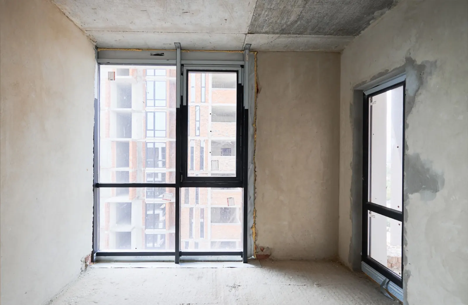 Zimmer im Rohbauzustand mit unverputzten Wänden und Betondecke, vor dem Ausbau